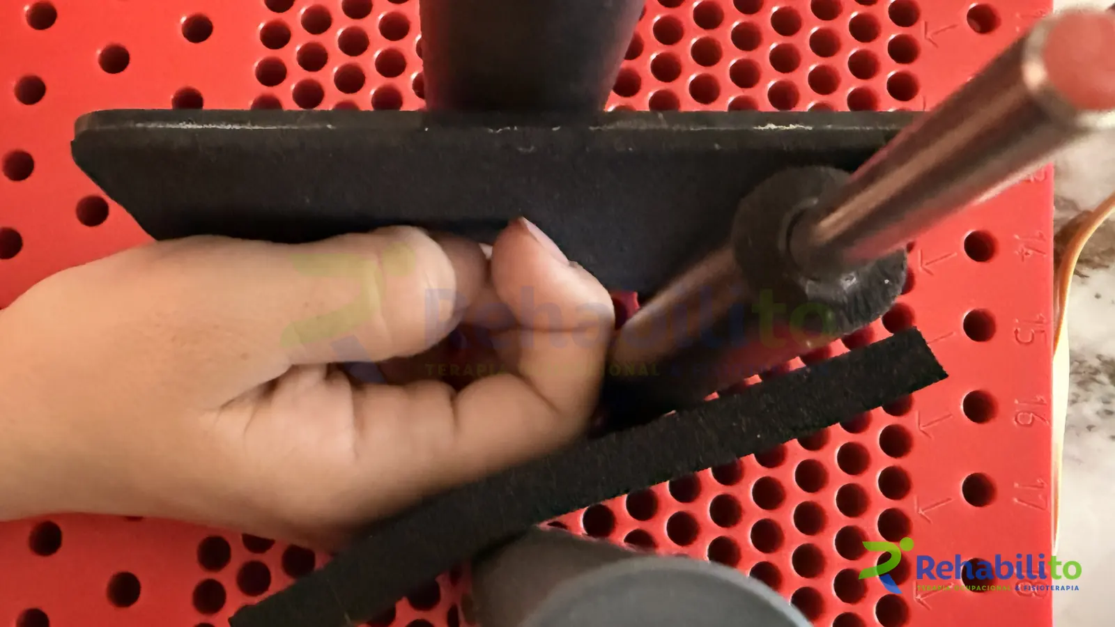 Mano en un ejercicio de agarre sobre una tabla canadiense roja con cilindros, terapia de mano