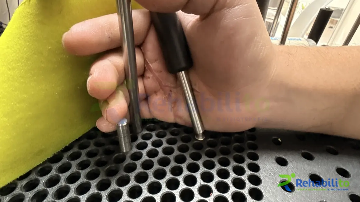 Mano sujetando cilindros metálicos sobre una tabla canadiense negra durante un ejercicio de pinza y agarre