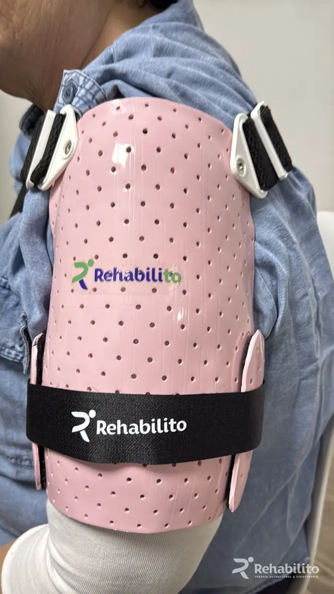 Paciente con una férula personalizada de hombro rosa perforada, sujeta con correas negras y anclajes blancos